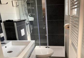 Bagno moderno con doccia in vetro, lavabo, WC, piastrelle nere e scaldasalviette in uno chalet.