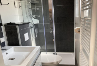 Modernes Badezimmer mit Dusche, Waschbecken, WC, schwarzen Fliesen und Handtuchheizkörper im Chalet.