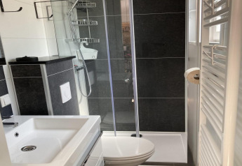 Baño moderno con ducha de cristal, lavabo, inodoro, azulejos negros y radiador en un chalet jardín.