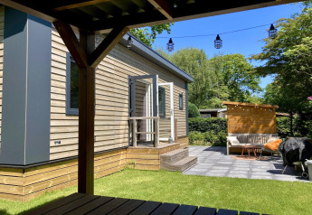 Chalet moderno con rivestimento in legno, giardino, terrazza e area salotto esterna in una giornata soleggiata nei Paesi Bassi.