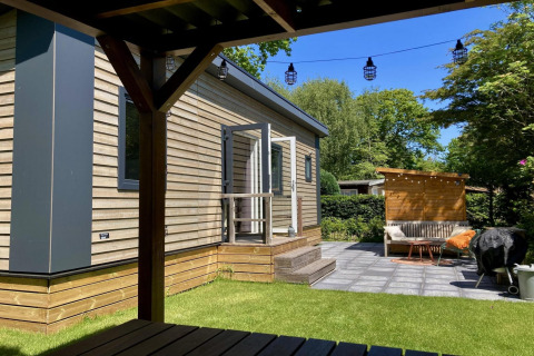 Moderne chalet med træbeklædning, have, terrasse og udendørs siddeplads på en solrig dag i Holland.