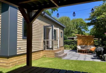 Modernes Chalet mit Holzverkleidung, Garten, Terrasse und Sitzbereich an einem sonnigen Tag in den Niederlanden.