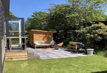 Modern chalet met tuin en terras in Nederland, zonnige zithoek met barbecue en groen gras.