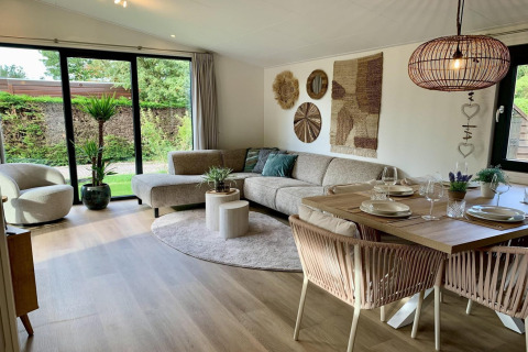 Salon moderne et cosy d’un chalet aux Pays-Bas, grand canapé d’angle, table à manger et grandes baies.
