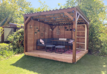 Chalet moderno in legno con terrazza coperta, giardino e area salotto accogliente in uno spazio soleggiato.