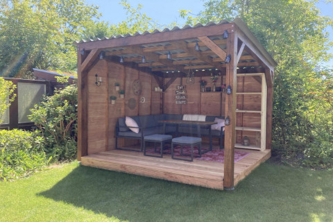 Moderne træhytte med overdækket terrasse, have og hyggelig siddeplads i solrige omgivelser.