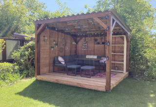 Chalet moderno in legno con terrazza coperta, giardino e area salotto accogliente in uno spazio soleggiato.