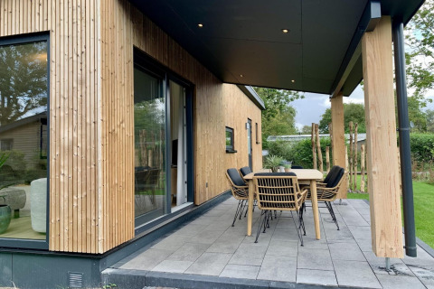 Chalet moderne en bois avec véranda couverte et coin repas extérieur, entouré de verdure aux Pays-Bas.