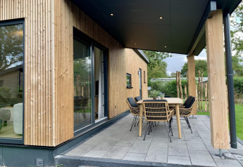 Moderno chalet de madera con veranda cubierta y muebles de exterior, rodeado de vegetación en Holanda.