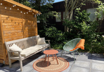 Terraza de chalet moderno en Países Bajos con banco, silla verde, mesa pequeña y cobertizo de madera.