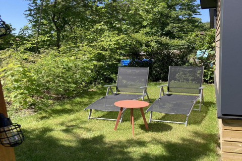 To liggestole og et lille bord på græsplænen ved siden af en moderne hytte med have og terrasse i Holland.