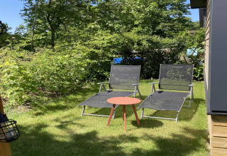 Deux transats et une petite table sur la pelouse à côté d’un chalet moderne avec jardin et terrasse aux Pays-Bas.