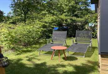 Dos tumbonas y una mesa pequeña en el césped junto a un moderno chalet con jardín y terraza en los Países Bajos.