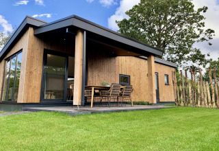 Modernes Holzchalet mit überdachter Veranda, Essbereich im Freien und Rasenfläche in den Niederlanden.