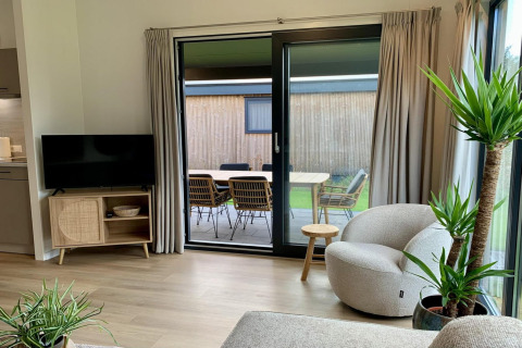 Soggiorno con arredi moderni, ampie vetrate e vista sul patio nel Pleasant chalet con veranda, Paesi Bassi.