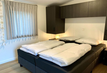 Chambre moderne de chalet aux Pays-Bas avec deux couettes sur un lit double et des armoires foncées.