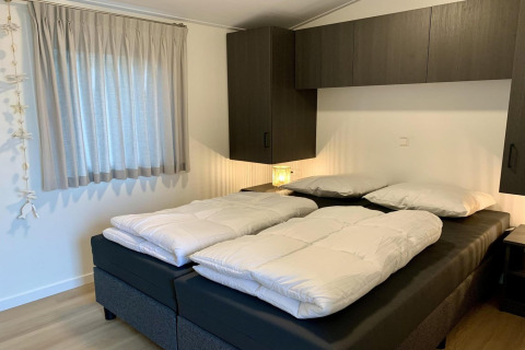 Moderne chalet slaapkamer in Nederland met twee eenpersoonsdekbedden en donkere kasten boven het bed.