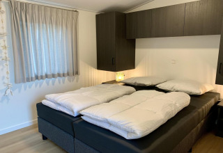 Chambre moderne de chalet aux Pays-Bas avec deux couettes sur un lit double et des armoires foncées.