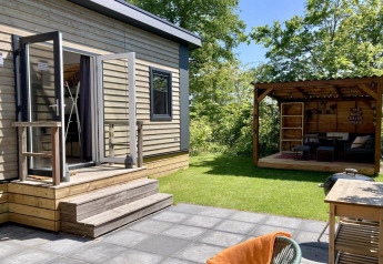 Modern chalet with a lush garden, terrace, and covered outdoor lounge area in the Netherlands, sunny day.