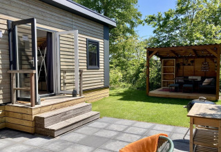 Chalet moderne avec jardin verdoyant, terrasse et coin salon extérieur couvert aux Pays-Bas, journée ensoleillée.