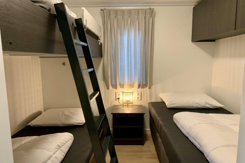 Slaapkamer met drie eenpersoonsbedden, een stapelbed, nachtkastje en lamp in Pleasant chalet met veranda.