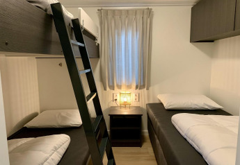 Værelse med tre enkeltsenge og en køje, et natbord og en lampe ved vinduet i Pleasant chalet med veranda.