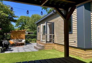 Modern chalet met tuin, terras en knusse zithoek, gezien vanonder een overkapping in Nederland.