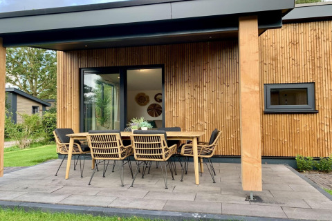 Veranda van de Pleasant chalet in Nederland met houten buitenkant en een tafel met acht stoelen.