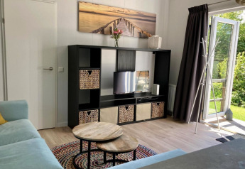 Soggiorno chalet moderno con scaffale nero, TV, tavolini rotondi e porta aperta sul giardino in Olanda.