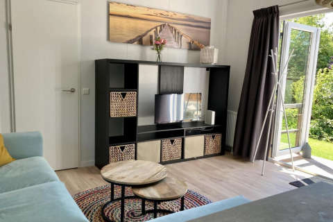 Moderne chalet living met zwarte kast, tv, ronde tafeltjes en open deur naar tuin in Nederland.