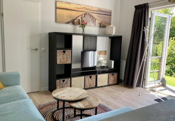 Moderne chalet-stue med sort reol, fladskærms-tv, runde borde og åben dør til have i Holland.