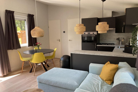 Modernes Chalet in den Niederlanden mit gelben Stühlen, Rattanhängelampen und gemütlicher Sitzecke.