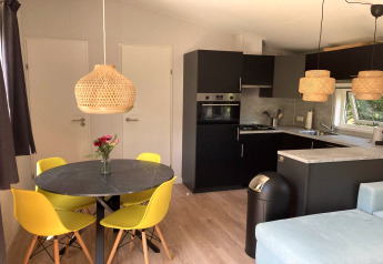 Chalet moderno nei Paesi Bassi con cucina nera, sedie gialle, lampade in vimini e pavimento chiaro.