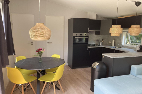 Modern chalet met zwarte keuken, gele stoelen, rieten lampen en lichte houten vloer in Nederland.