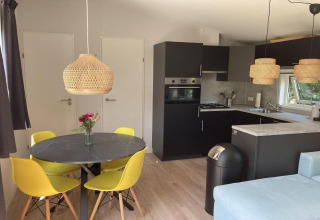 Modern chalet in Nederland met zwarte keuken, gele stoelen, rieten lampen en licht houten vloer.