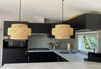 Modern chalet kitchen in the Netherlands with dark cabinets, woven pendant lights and garden view window.