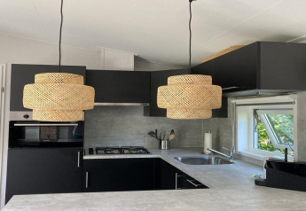 Moderne chaletkeuken in Nederland met donkere kasten, gevlochten hanglampen en raam op de tuin.