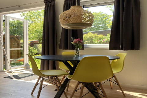 Interior luminoso de chalet moderno con sillas amarillas, mesa negra y vistas al jardín desde la puerta.