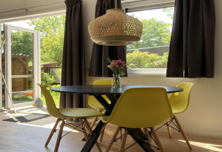 Interno di chalet moderno con sedie gialle, tavolo nero, lampada a sospensione e vista sul giardino.