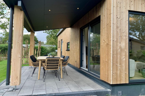 Überdachte Terrasse mit Esstisch und modernen Stühlen am Holzchalet in den Niederlanden.