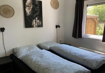 Soveværelse i moderne chalet i Holland med to enkeltsenge, vægkunst og vindue med udsigt til haven.