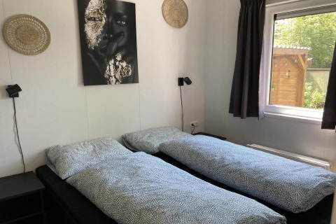 Schlafzimmer im modernen Chalet in den Niederlanden mit zwei Einzelbetten, Wandkunst und Gartenblick.