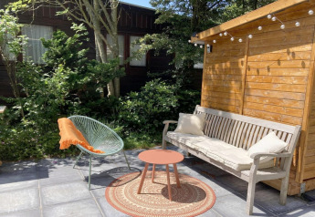 Udendørs terrasse ved moderne chalet i Holland med bænk, stol, rundt bord og hyggelig have.