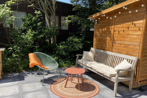 Udendørs terrasse ved moderne chalet i Holland med bænk, stol, rundt bord og hyggelig have.