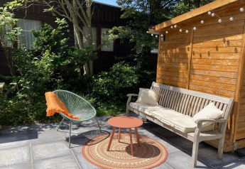 Outdoor terrace at a modern chalet in the Netherlands featuring a bench, chair, small table, and garden.