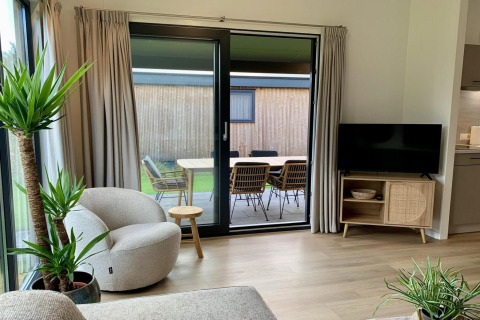 Lichte, moderne woonkamer in chalet met schuifdeur en uitzicht op terras met eettafel buiten.