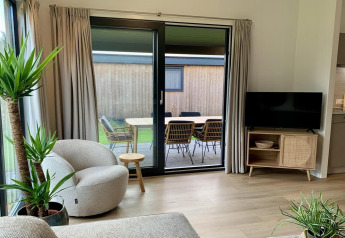 Lyst og moderne opholdsområde i et chalet med store glasdøre, udsigt til terrasse og udendørs bord.
