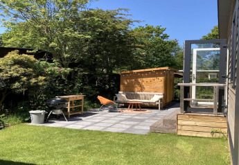 Moderner Garten mit Terrasse, Grill und Sitzbank am Chalet, sonnig und grün in den Niederlanden.