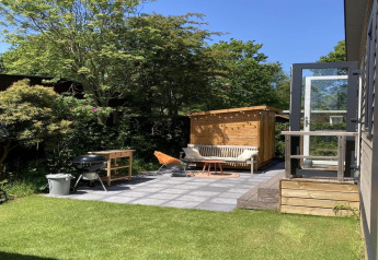 Moderner Garten mit Terrasse, Grill und Sitzbank am Chalet, sonnig und grün in den Niederlanden.