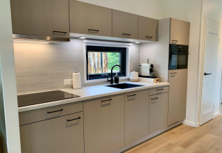 Moderne keukeninrichting in Pleasant chalet met veranda in Nederland, met veel kastruimte en raam.